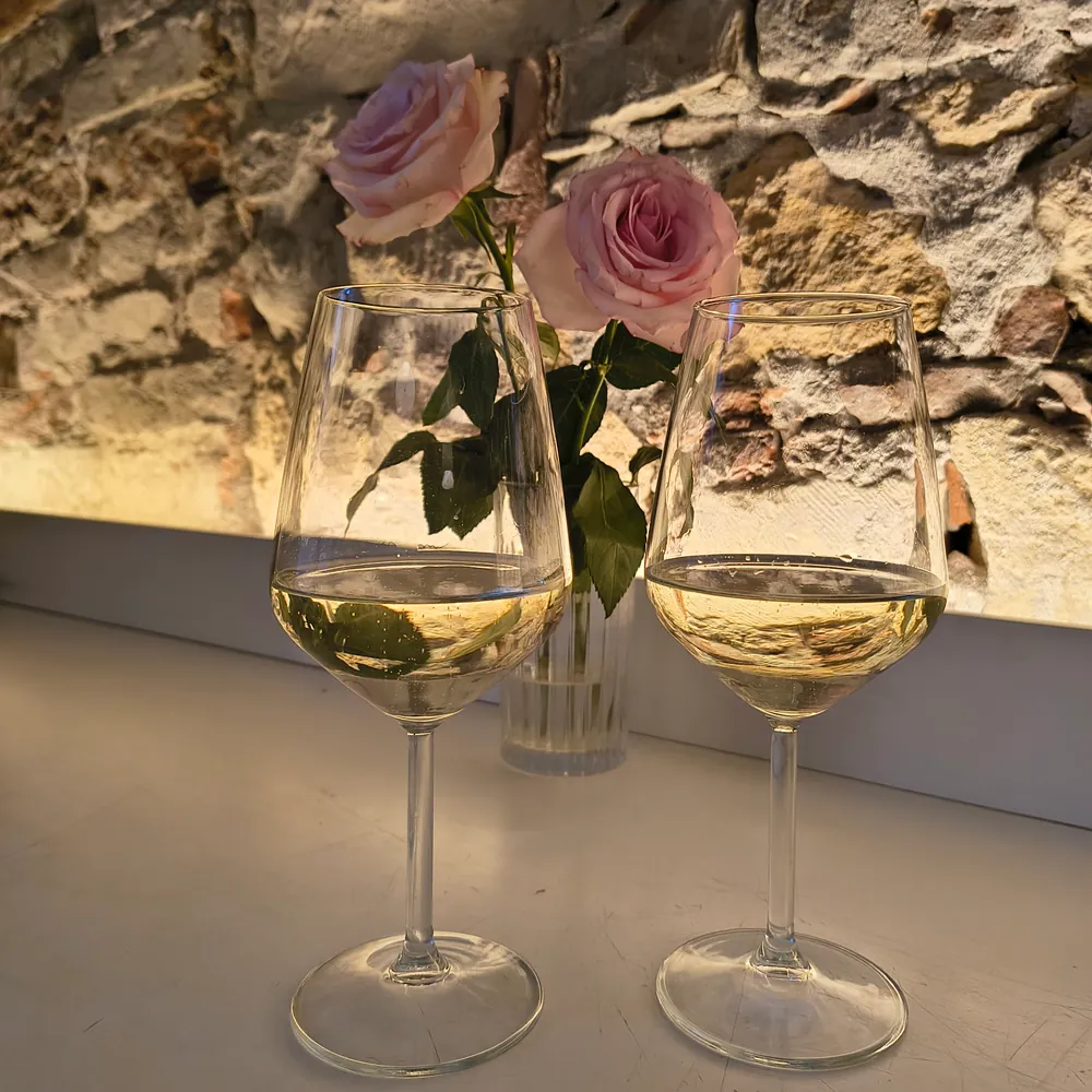 Two glasses of Prosecco in front of the stone wall, with pink roses in a vase