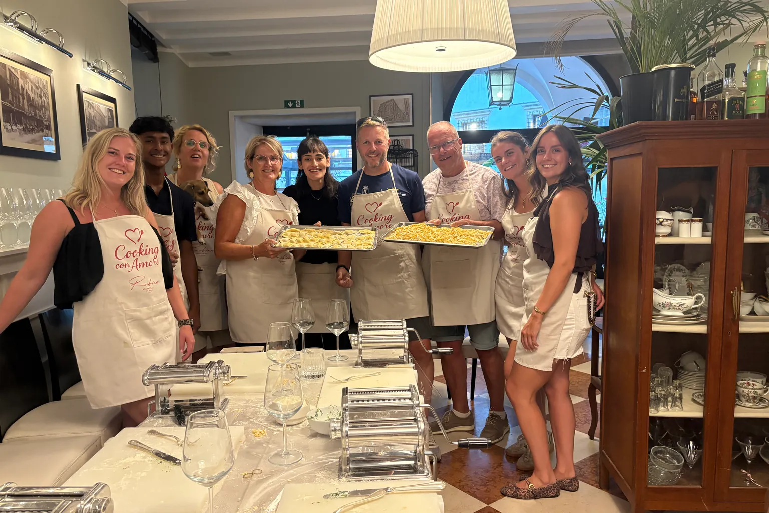 Guests in Cooking con Amore aprons hold up trays of the pasta they made