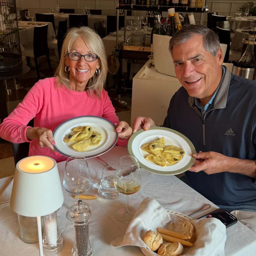Two guests at the table show plates of the ravioli they made, with wine glasses in front of them